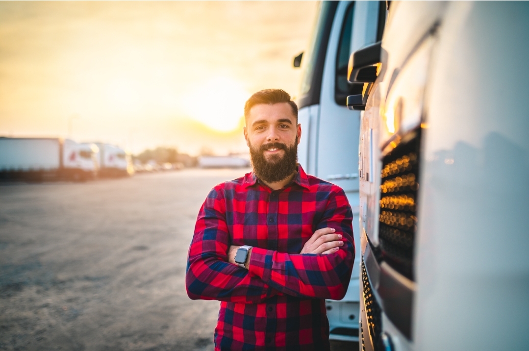 Professional truck driver standing beside the cab of a semi truck at sunset
